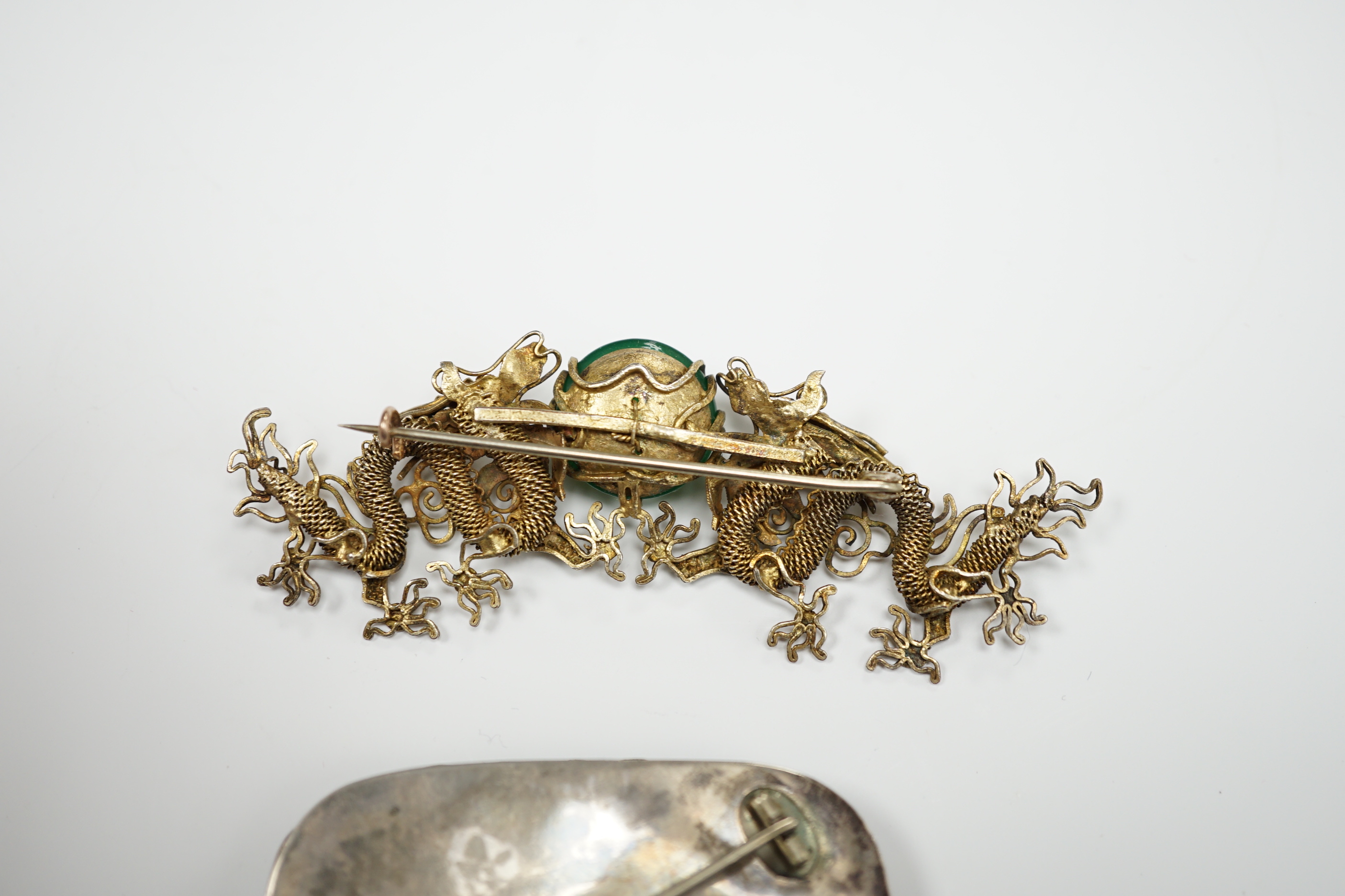 A Chinese? white metal and polychrome enamelled brooch, depicting a hare amongst foliage, 59mm(a.f.), together with a similar gilt white metal filigree and cabochon green paste set brooch.